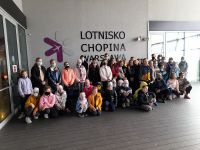 Grupa uczniów stoi w pomieszczeniu na tle napisu Lotnisko Chopina w Warszawie